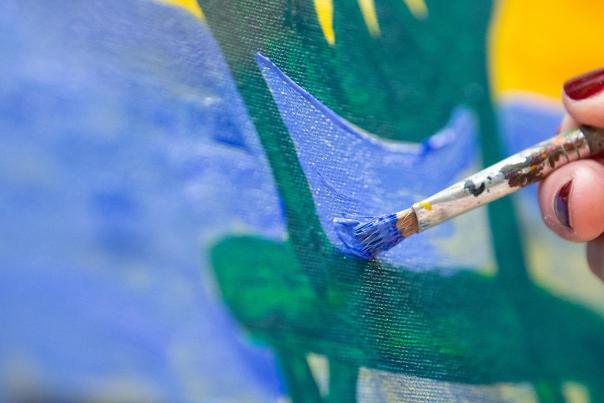 A white hand holds a paint brush and brushes blue on a canvas
