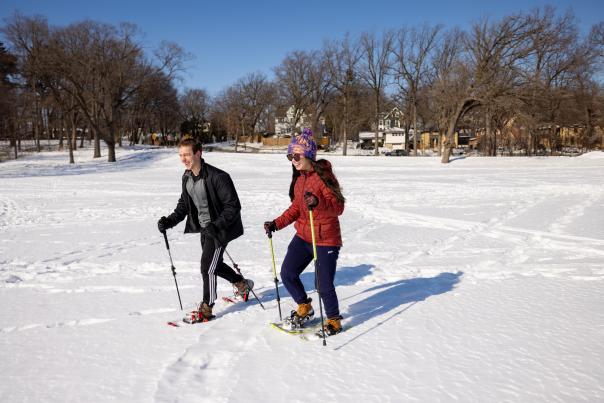 A couple snowshoeing over a frozen lake covered in snow on a sunny winter day.