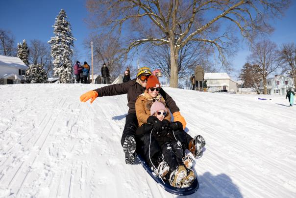 Two parents and their kid are bundled up in winter gear as they sled down a snow covered hill.