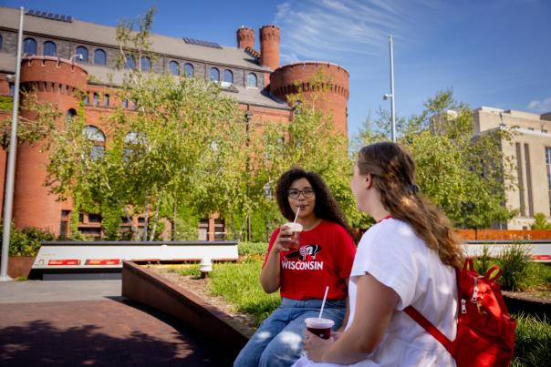 A Black woman and a white woman sit outside of the Red Gym on the UW Campus while they sip smoothies.