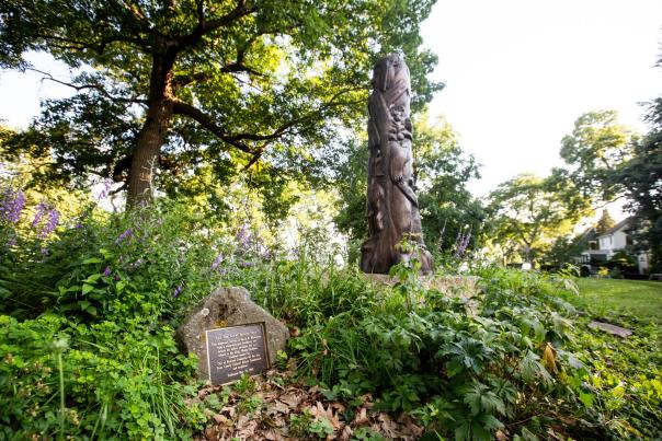 A totem pole featuring bears carved from wood sits near a historical marker identifying a Ho-Chunk effigy mound in Madison, WI
