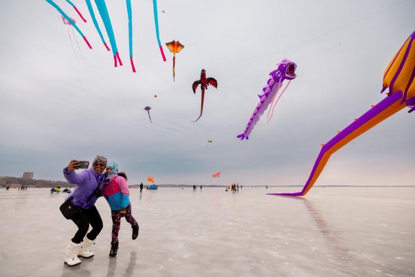 A black woman and her daughter taking a selfie in front of the kite show at the Frozen Assets Festival on Lake Mendota.
