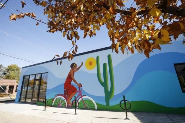 A mural on the side of a building of a Black woman riding a bicycle in the sun.