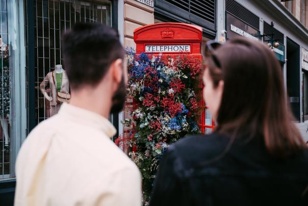 2 people looking at a red phonebox decorated with flowers for the Manchester Flower Festival