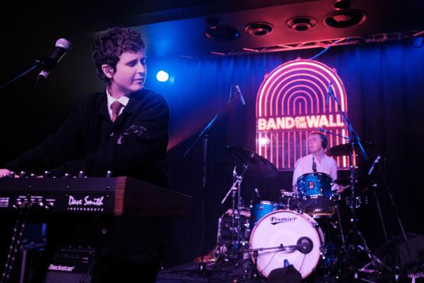 Band on stage in front of neon Band on the Wall sign