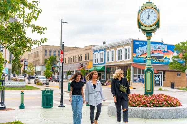 three women walking in downtown Manitowoc by the clock at Burger Boat Park