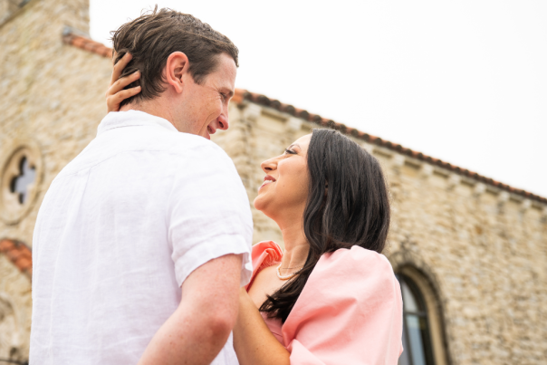 Couple gazing at each other with a historic chapel in the background under gray skies