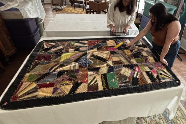 Two people looking at a historic crazy quilt with a wild pattern