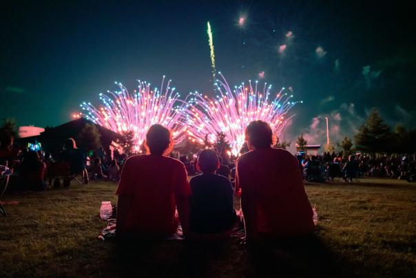 silhouettes of three people (a family) sitting with fireworks going off in front of them.