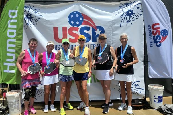 Group of people posing with pickleball paddles and medals around their necks at the US Senior Pickleball tournament