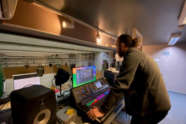 A white man with dark bear & pony tail standing at a mixer desk to do the AV at Fitzwilliam College Cambridge