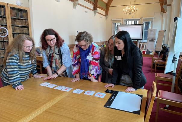 5 white women leaning over a wooden table looking at a series of cards as part of a team building activity in Cambridge