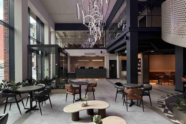 Modern hotel lobby at Aloft Manchester City Centre featuring high ceilings, large windows, contemporary seating areas and a central bar space with stylish lighting.