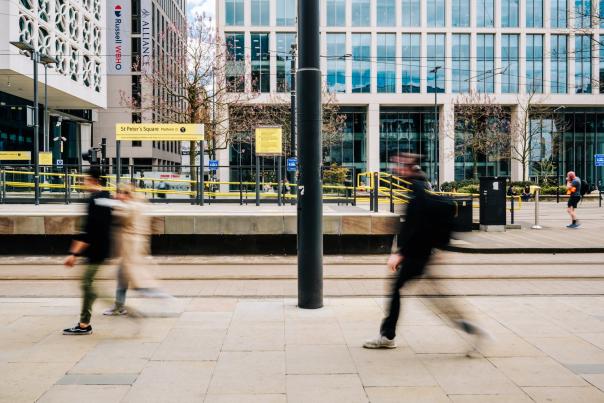 People walking in front of camera in city centre with tram stop and buildings in the background