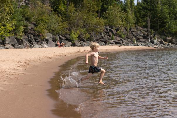 A boy running into the water at the beach at Marquette Harbor Lighthouse, located in the Upper Peninsula of Michigan