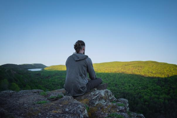 A person meditating on a rock outcrop overlooking a forest in the Upper Peninsula of Michigan