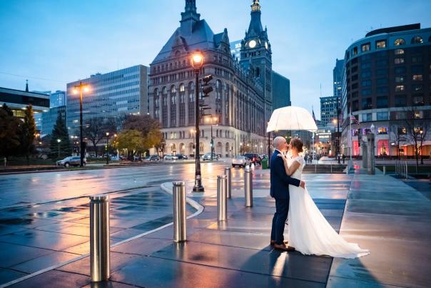 a bride and groom under an umbrella on a city sidewalk