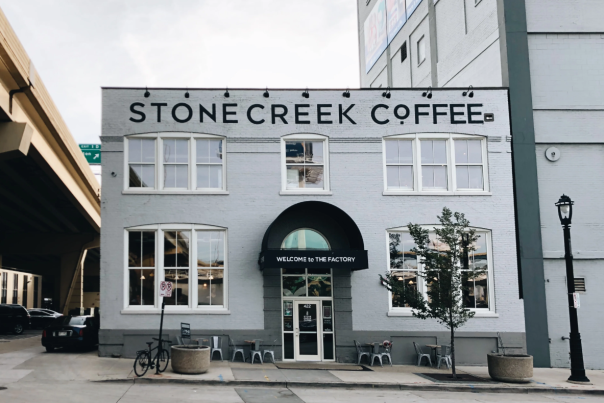 Exterior of Stone Creek Coffee’s white brick building with large front windows, black awning, and outdoor seating along the sidewalk.