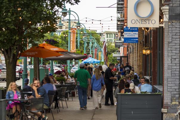 Diners fill outdoor patio tables along a tree-lined Historic Third Ward sidewalk, while pedestrians walk past restaurants and storefronts under hanging string lights.