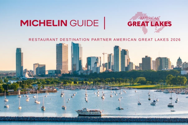 A waterfront view of Milwaukee’s skyline at sunset, with sailboats docked in the marina and a tour boat moving across Lake Michigan in the foreground. Above the skyline, red text reads “Michelin Guide | American Great Lakes” with the subheading “Restaurant Destination Partner American Great Lakes 2026.”