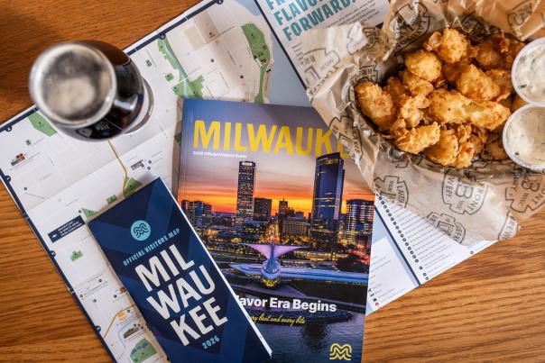 The 2026 Milwaukee Official Visitors Guide and Official Visitors Map are displayed with a beer and cheese curds on a table.