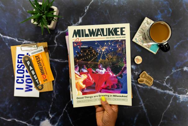 layflat of Milwaukee visitors guide held up over an array of milwaukee items