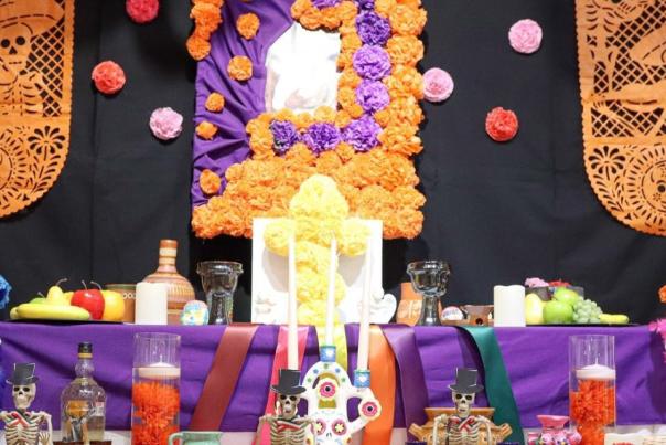 Colorful Día de los Muertos ofrenda decorated with marigolds, papel picado, candles, fruit and skeletal figures.