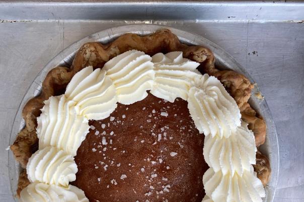 Whole pie with a golden brown filling topped with piped whipped cream and coarse sugar crystals in a flaky crust on a metal tray.