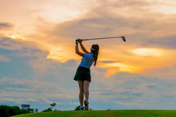 A golfer teeing off into the distance while the sun sets in the horizen