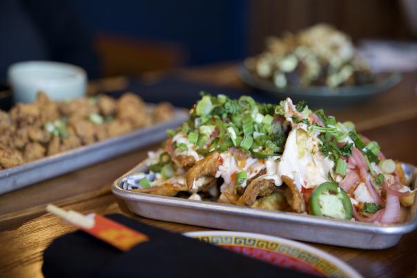 Plate of crab rangoon nachos from Slurp Society sitting on a table near other appetizers.