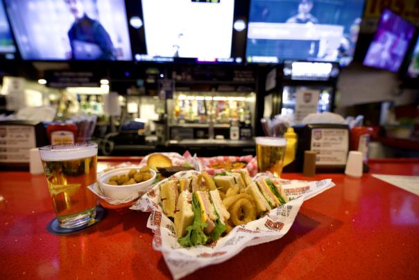 Glass of beer and sandwich platter sitting on bar.