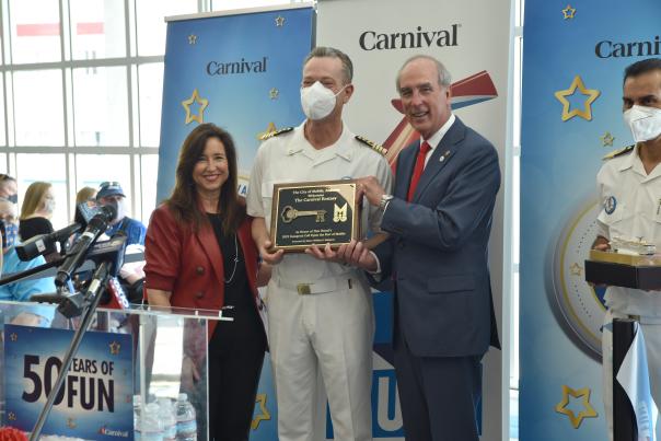 Three people posing with a plaque in front of Carnival Cruise banners