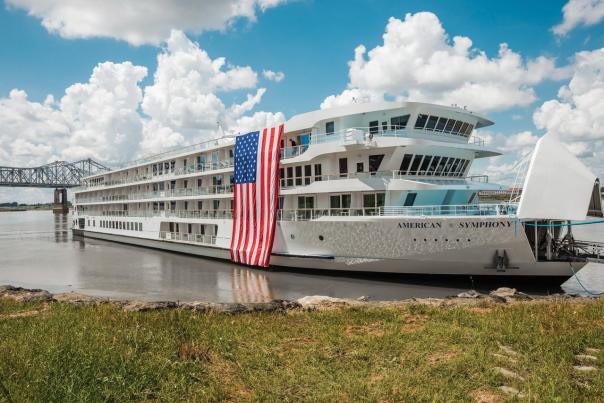 American Cruise Lines' Symphony, a Mississippi riverboat, is in port with an American flag draped down the side.