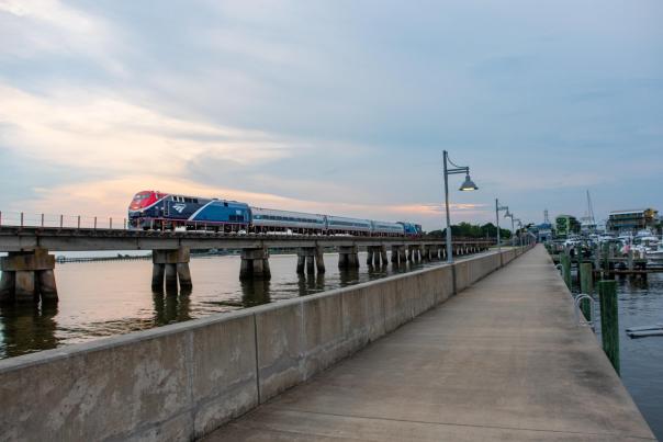 The Amtrak Mardi Gras Service train travels over a concrete bridge above the water.