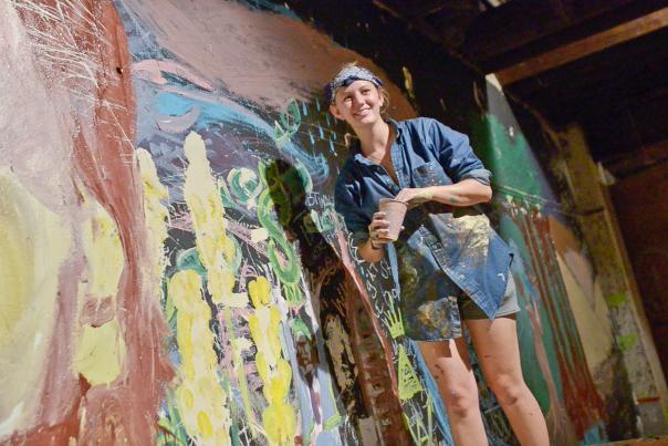 female artist painting a wall mural with her hands