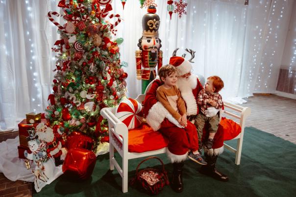 Two redheaded boys sit on Santa's lap on a bench in front of a Christmas tree