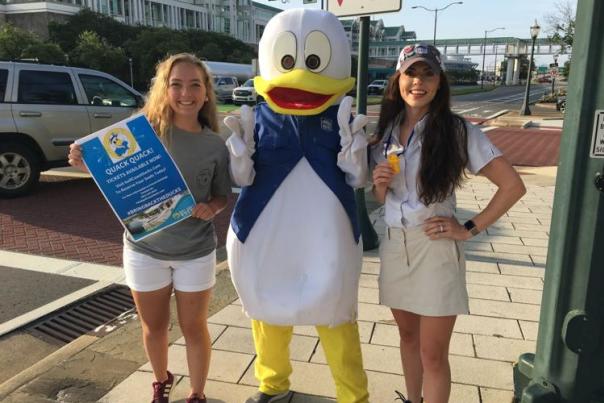 two women posing with a person in a large duck costume