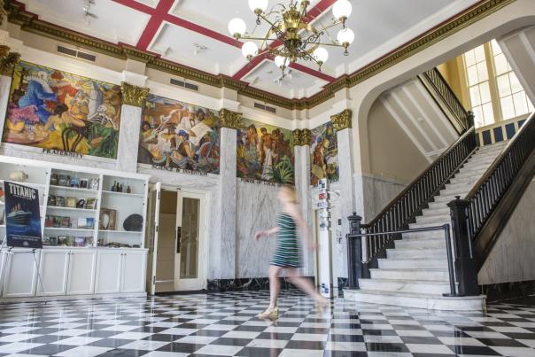 Woman in a blue dress crosses the lobby in front of a white marble staircase