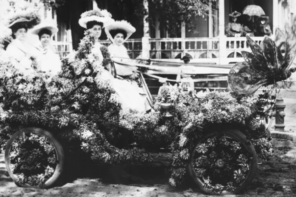 black and white photo of four ladies riding in an antique car decorated with flowers