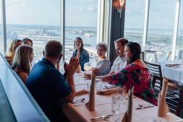 Eight men and women smile and talk at a restaurant overlooking Mobile River