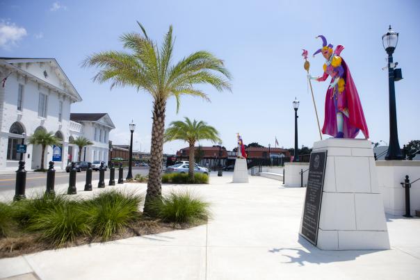 statue of Mardi Gras statue on sidewalk with palm tree beside it
