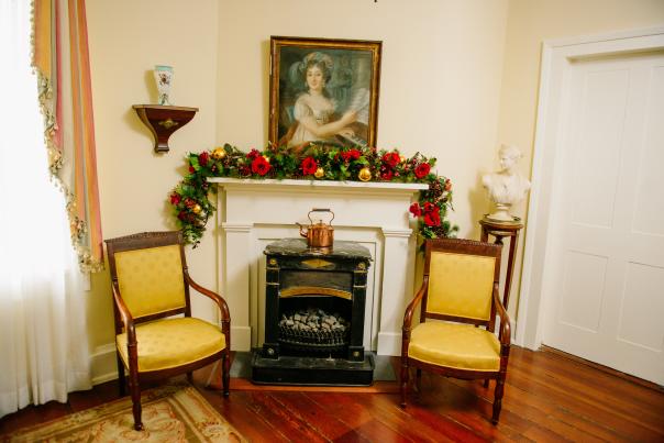 two chairs on either side of a fireplace with holiday decoration in a historic home