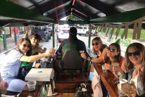 group of five people bicycling on a party bike with drinks
