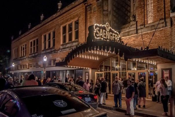 building with lighted entrance at night, people and cars outside