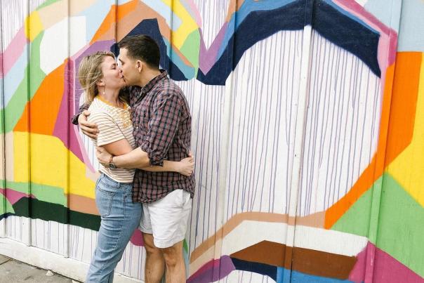couple kissing in front of rainbow heart mural