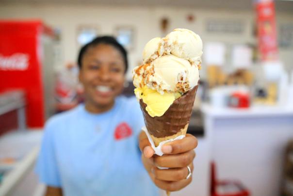 girl holding up a triple scoop ice cream in a waffle cone