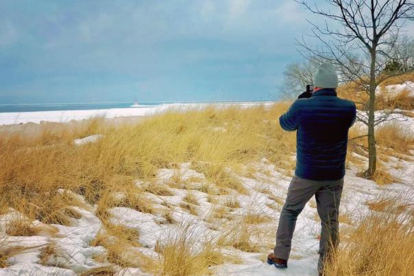 man on snow dune taking picture of lake michigan