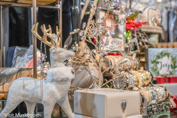 store holiday display of of white and sparkly deer with fur collar and gold antlers stands before display of shiny bracelets and leather purse and box