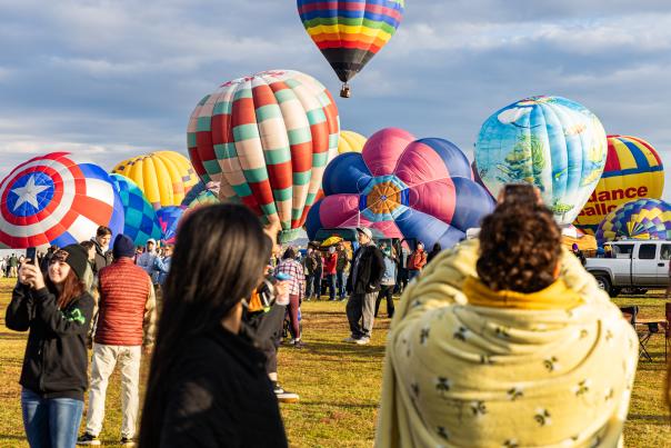 picture of hot air balloons taking flight during Balloon Fiesta with spectators watching and taking pictures