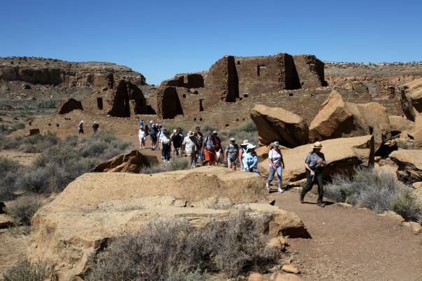 A Group Of People Walking Single File Through Chaco Canyon